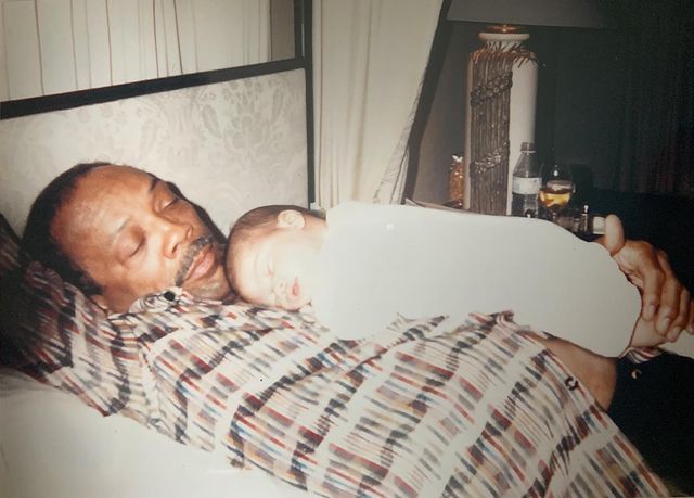 Kenya Kinski-Jones laying on her father's, Quincy Jones' chest when she was 1 year old. Quincy is wearing check shirt and Kenya is wraped by a white cloth. We can see them living loving each other.